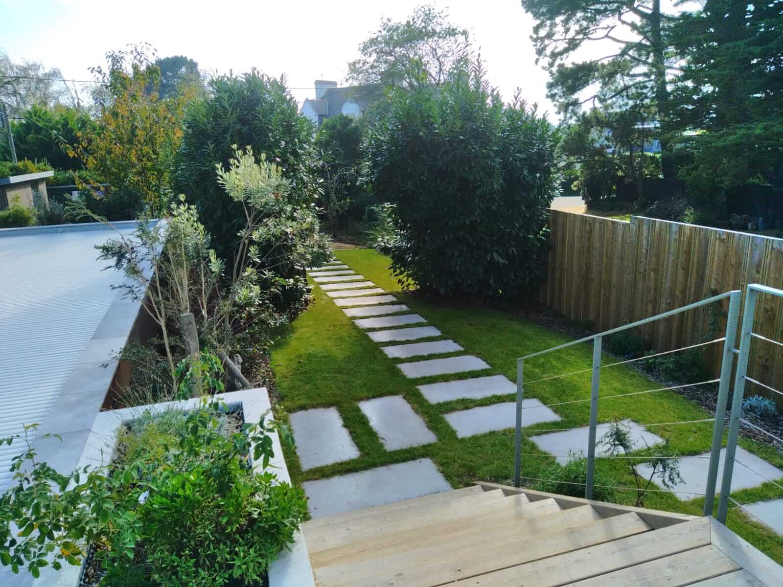 Allée de jardin avec dalles en béton et bordée de plantes avec escalier en bois