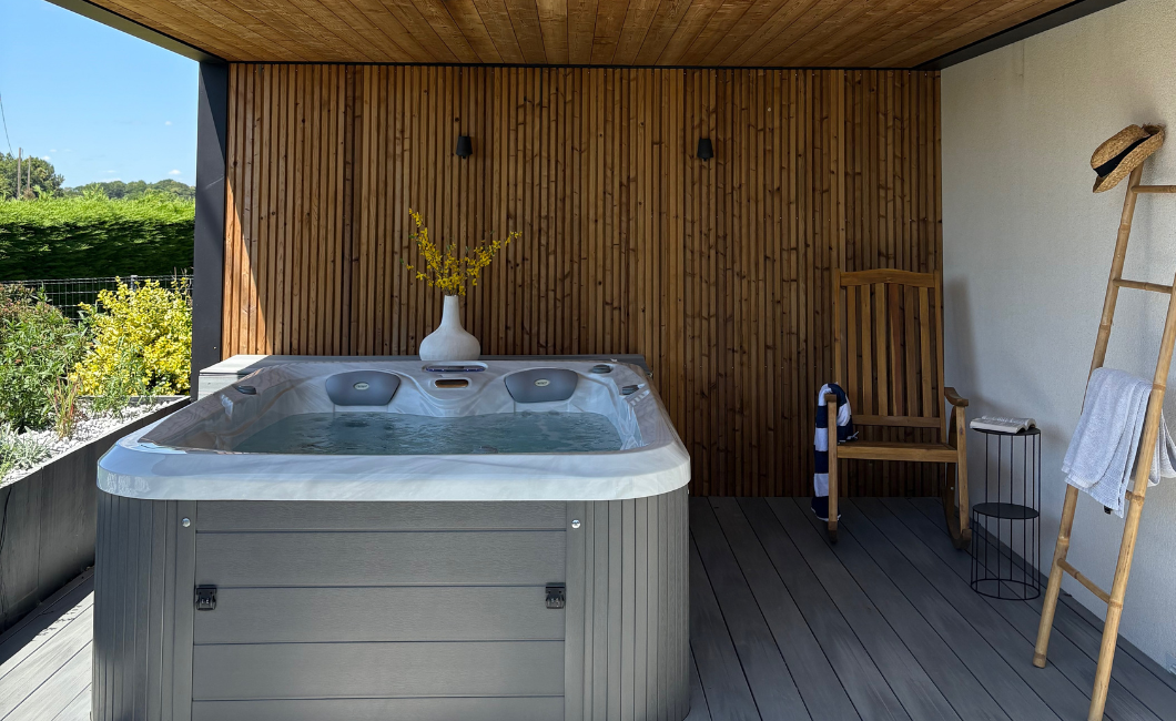 Spa extérieur sous pergola contemporaine en aluminium noir avec habillage bois vertical et terrasse composite.